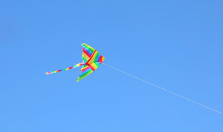 rainbow-colored kite flying high in the sky symbolizing freedom and youthful carefreenessの写真素材