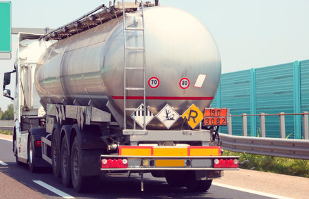 fuel tanker speeding along highway noise barriers with hazardous material r sign on the roadの写真素材