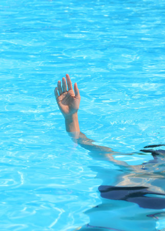 girl's hand reaching out from deep pool water signaling for helpの写真素材