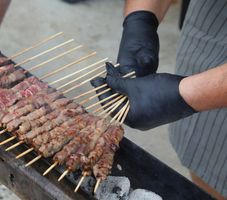 gloved hands of the cook turning skewers of sheep and mutton meat called arrosticini typical of Italian cuisineの写真素材