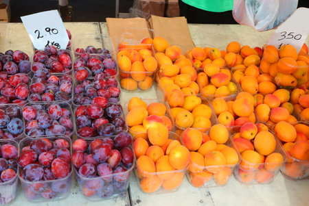 baskets with fresh plums and also orange apricots for sale at the greengrocer's stall at the market with price tagの写真素材