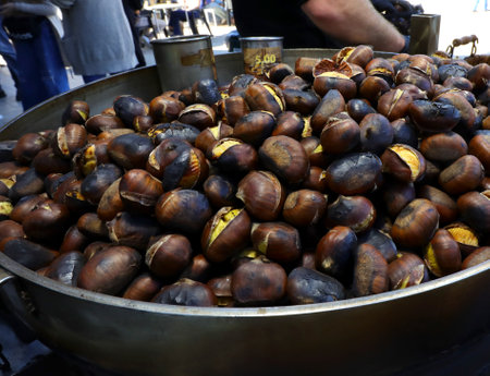 Roasted chestnuts cooked in a metal pan sold at a street food stall during autumn in the city streetsの写真素材
