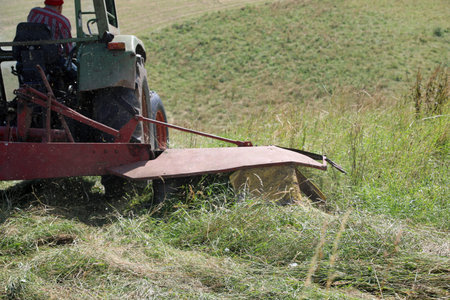Tractor in a field of cut grass and a rotary tiller aerating the soil after mowing