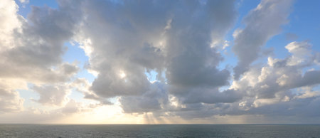 captivating wide-angle view of the sun filtering through low clouds at sunset, with the sea below