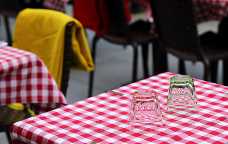 two glass tumblers sit on a table with a red and white checkered tablecloth at an alfresco cafeの写真素材