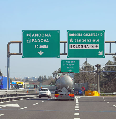 large highway signs on the Italian road with the junction to go to Ancona, Padua, Bologna or the ring road and airport and cars and a tankerの写真素材