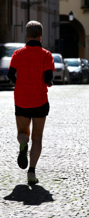 Athletic runner in backlight trains running through the streets of the city with cobblestone pavingの写真素材