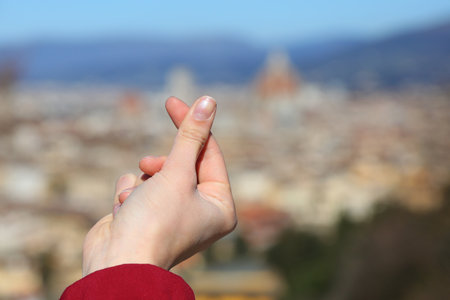 Hand of a young girl who with her thumb and forefinger forms the sign of the Heart and the Italian city of Florence in the blurred backgroundの写真素材