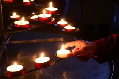 wax candles and the hand of the young woman who lights a candle as a sign of hope and prayer during the religious ceremony in the religious templeの写真素材