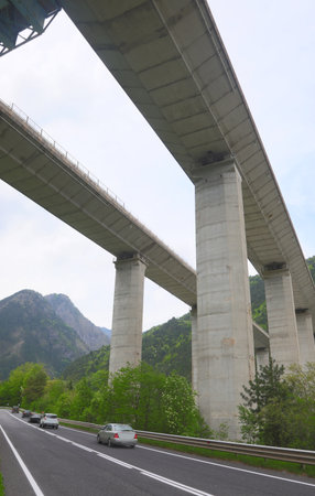cars running on the road under the highway viaduct supported by gigantic pylons of concreteの写真素材
