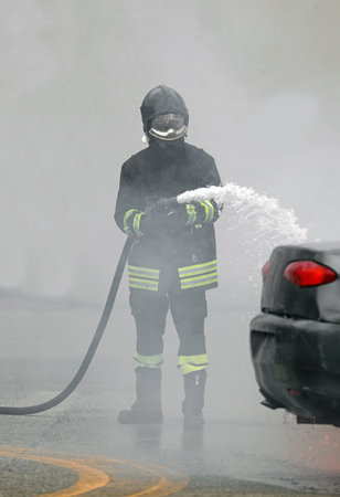 Firefighter with the fire hose in the white smoke of the fire after the road accidentの写真素材