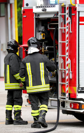 Two firefighters with protective helmets and uniform during emergency management and the fire truck