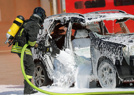 Firefighter with the protective helmet and oxygen cylinder while spraying the foaming coat to...