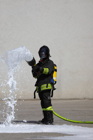 brave firefighter with big fire hose and foam and protective helmet and breathing apparatus oxygen...