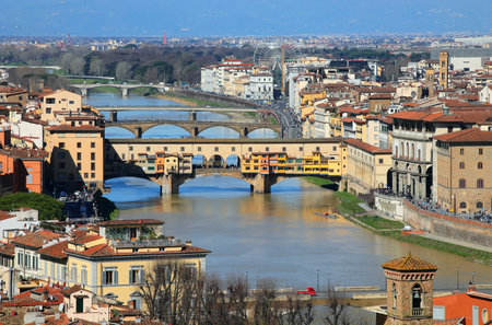 Aerial view of the Ponte Vecchio over the Arno river perfectly illuminated by the sun and other historic buildings in Florence in ITALYの写真素材