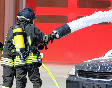 Two firefighters while spraying foamy white extinguishant on the car after the road accidentの写真素材