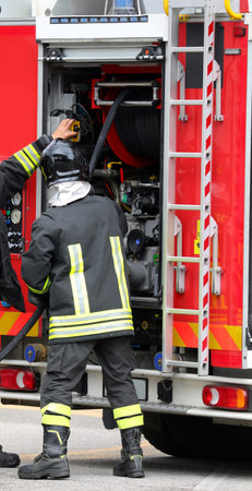 firefighters in protective helmets and uniform unroll fire hose during emergency management and pump...