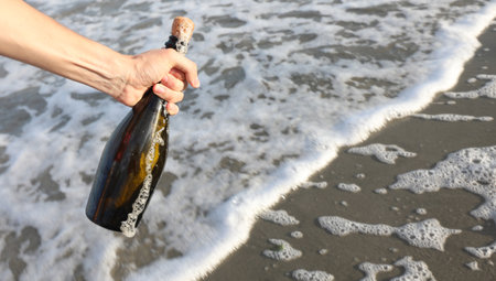 mans hand that found glass bottle with secret message inside on seashoreの写真素材