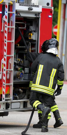firefighters with uniforms and protective helmets and fire trucks in action during emergency in city