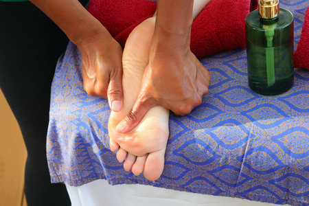 womans hand applying strongly thumb pressure to a girls foot soles on a massage bed with scented oil dispenser for therapeutic and beauty massagesの写真素材