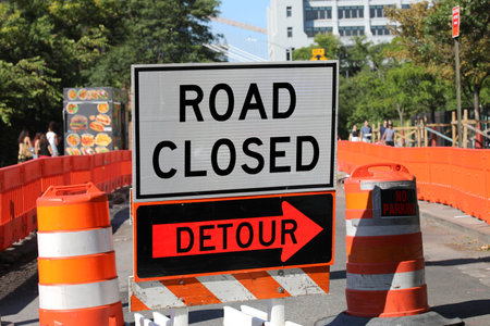 road closed sign with a detour arrow and orange construction barrels on a city street