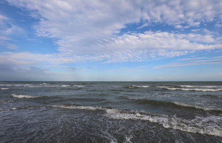 sea with few waves on the shore and blue sky with white clouds ideal for relaxation and maritime...