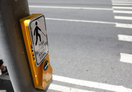 yellow pedestrian button on a metal pole on a sidewalk next to a traffic lightの写真素材