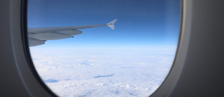 wing of the airplane and the white clouds from above seen from the small window porthole