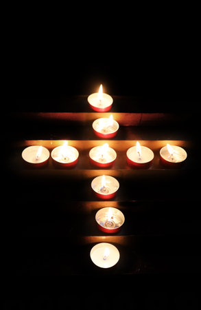 Many burning prayer candles arranged as a cross holy sign against a dark sanctuary backdropの写真素材