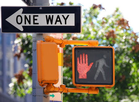 directional marker displaying one way and the illuminated red walk signal in new york cityの写真素材