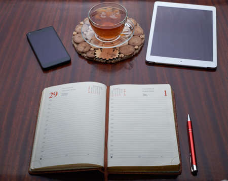 On the wooden table is a plate, a cup of tea, a cell phone, Address Book, Pen, Dolarの写真素材