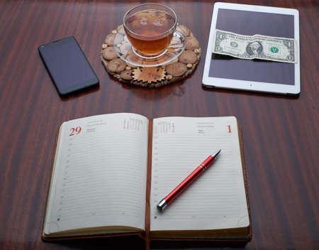 On the wooden table is a plate, a cup of tea, a cell phone, Address Book, Pen, Dolar, moneyの写真素材