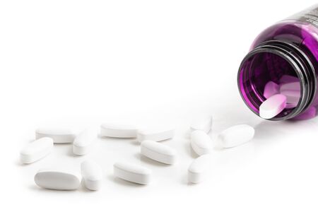 Medication bottle and white pills spilled on white backgroundの写真素材