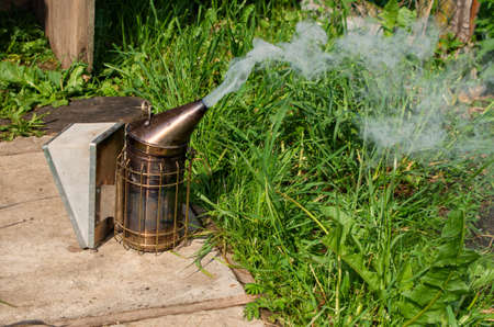 Old Smoker standing on the hive. A bee smoker is a device used in beekeeping to calm honey bees. It is designed to generate smoke from the smouldering of various fuels, hence the name.の写真素材