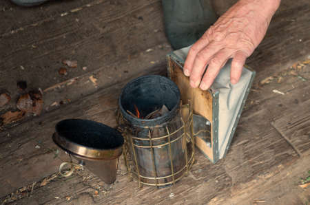Old Smoker standing on the hive. A bee smoker is a device used in beekeeping to calm honey bees. It is designed to generate smoke from the smouldering of various fuels, hence the name.の写真素材