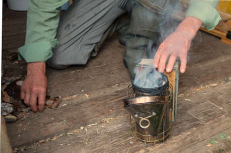 Old Smoker standing on the hive. A bee smoker is a device used in beekeeping to calm honey bees. It is designed to generate smoke from the smouldering of various fuels, hence the name.の写真素材