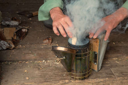 Old Smoker standing on the hive. A bee smoker is a device used in beekeeping to calm honey bees. It is designed to generate smoke from the smouldering of various fuels, hence the name.の写真素材