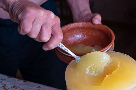 Person spoon to scoop honey from a large pot. A man shifts the honey in a clay plate in the kitchen.の写真素材