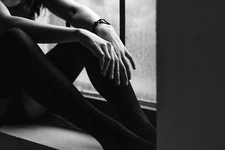 A girl in a white T-shirt and jeans with a bracelet crocheted squats, studioの写真素材