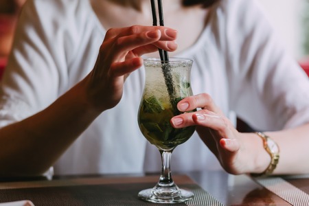 A young pretty womancafe drinks a mahita cocktail through a straw from a misted glass, outdoor hipster portraitの写真素材