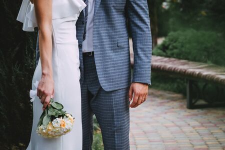 Newlyweds, before the wedding, in love, took each other's hands, Newlyweds hold hands next to the wedding rings that lie on the mirror surface near the tender wedding bouquetの写真素材