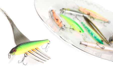 Fork with artificial fishing bait, similar lures lie on porcelain plateの写真素材