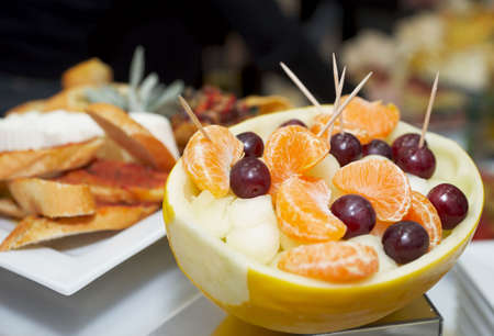 Melon stuffed with melon pieces, tangerine and grapes, other snacks in backgroundの写真素材