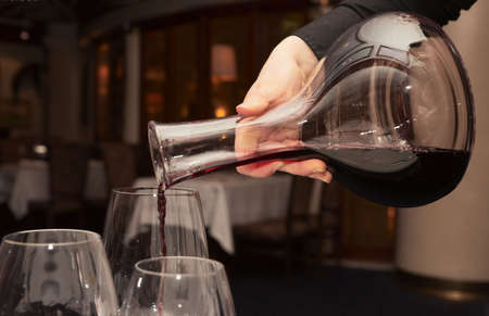 Waiter pouring red wine from decanter in dark restaurantの写真素材