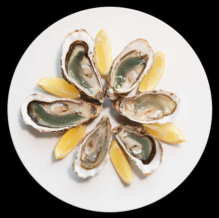 Fresh oysters on plate with lemon isolated on black baclgroundの写真素材