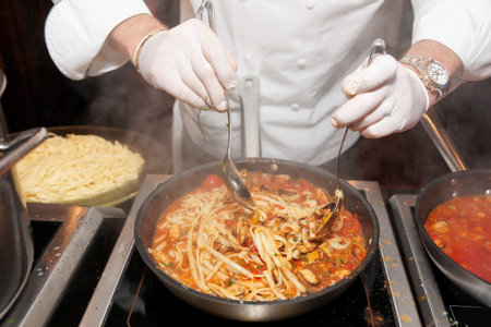 Chef frying mussels with pasta on commercial kitchen in restaurant. Chef's watch TM cloned out