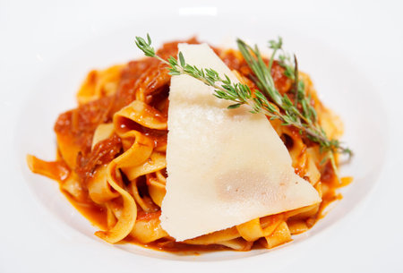 Pasta with tomato sauce, slice of parmesan, thyme and rosemary in plate, close-upの写真素材