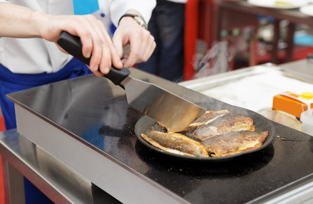 Chef frying seabass fillet in pan on commercial kitchen