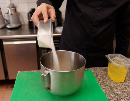 Pastry chef is pouring sugar in a mixing bowl to make a creamの写真素材