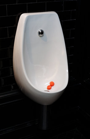 Urinal bowl with antiseptic tablets in dark black tiled restroom